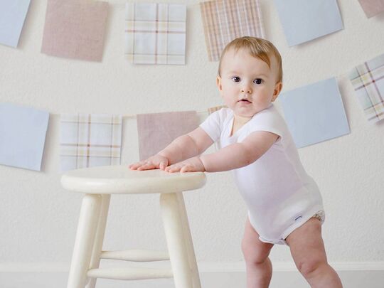 Enfant debout se tenant à un tabouret.